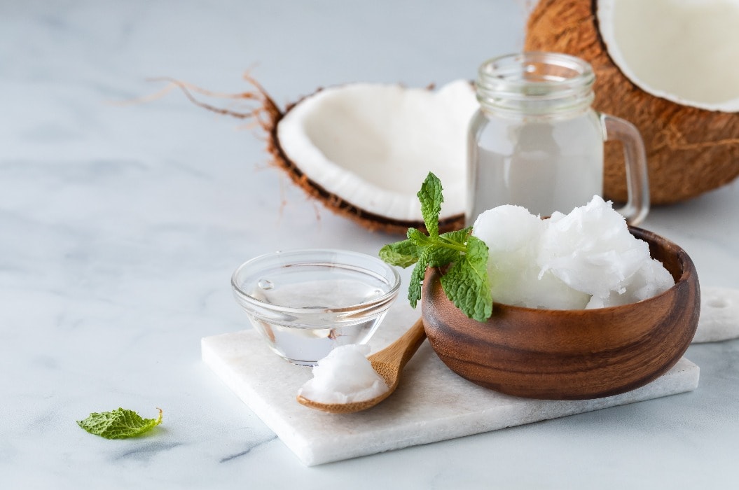 Close up of coconut oil along with coconut water and a coconut cracked in half in behind.