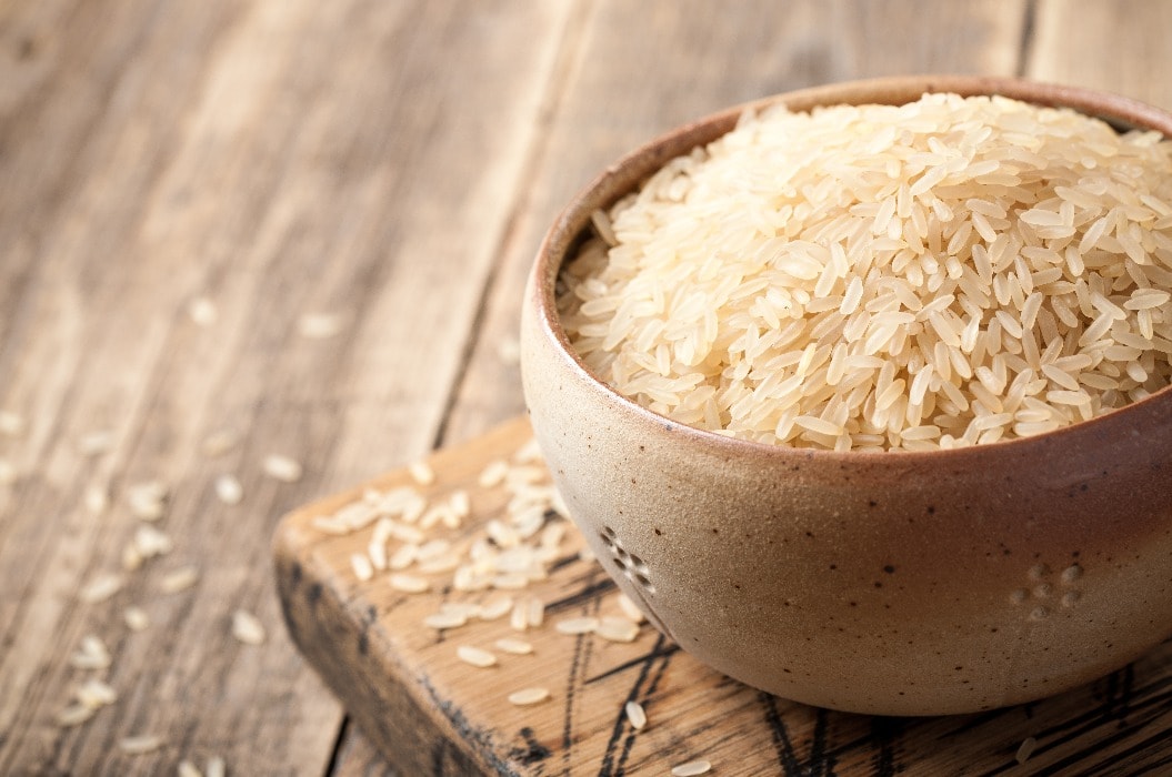 Uncooked parboiled rice in a bowl on wooden table